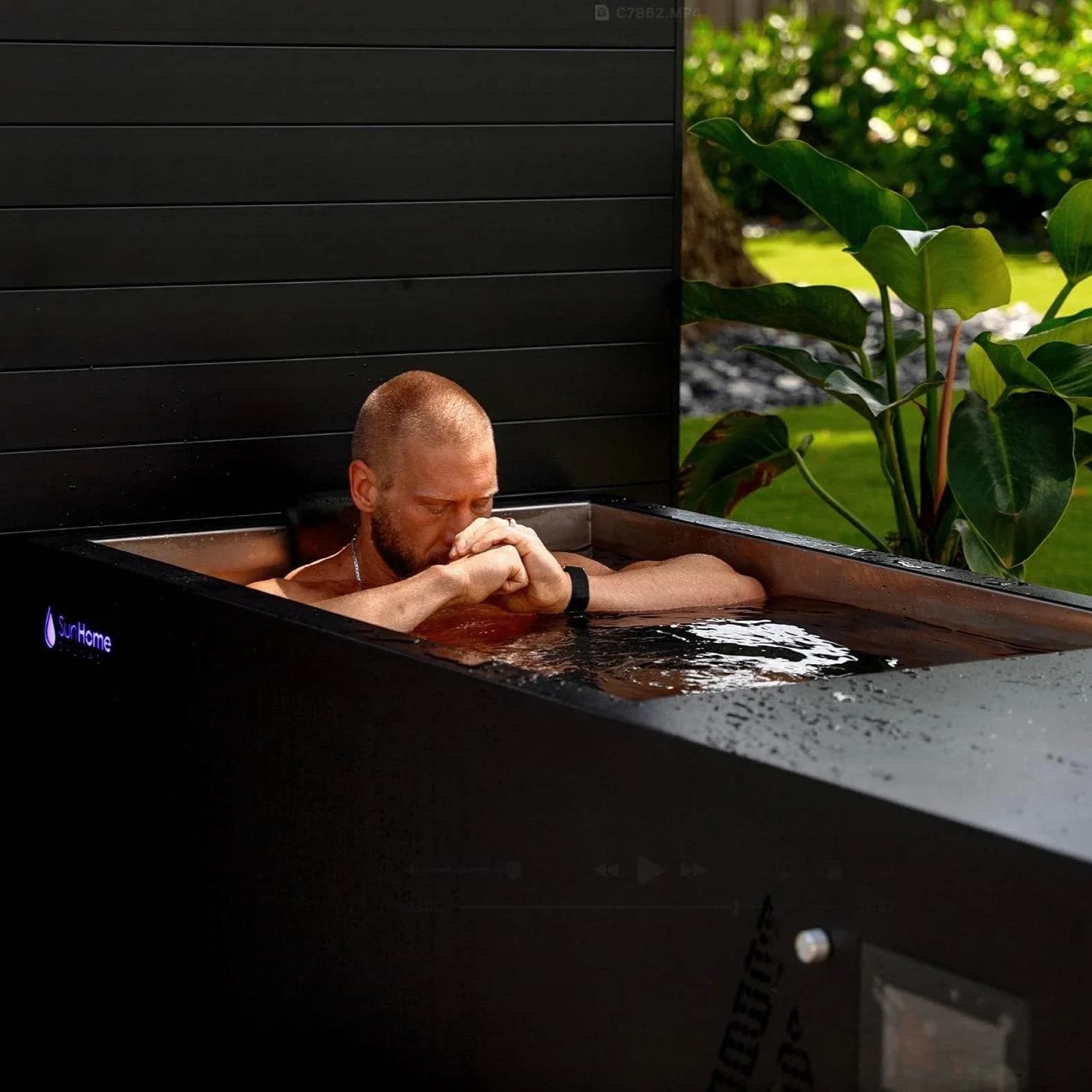 Man soaking in the Sun Home Cold Plunge Pro beside a plant