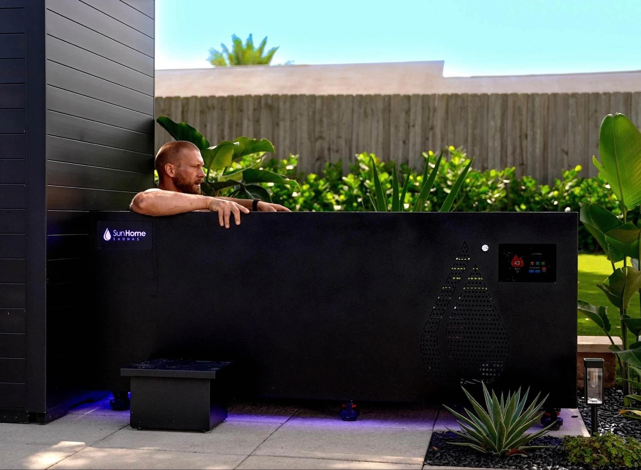 Man resting on the rim of the Sun Home Cold Plunge Pro in a backyard