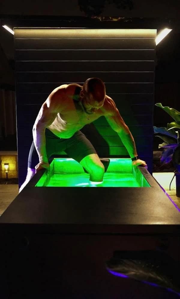 Man stepping into the lit Sun Home Cold Plunge Pro at night